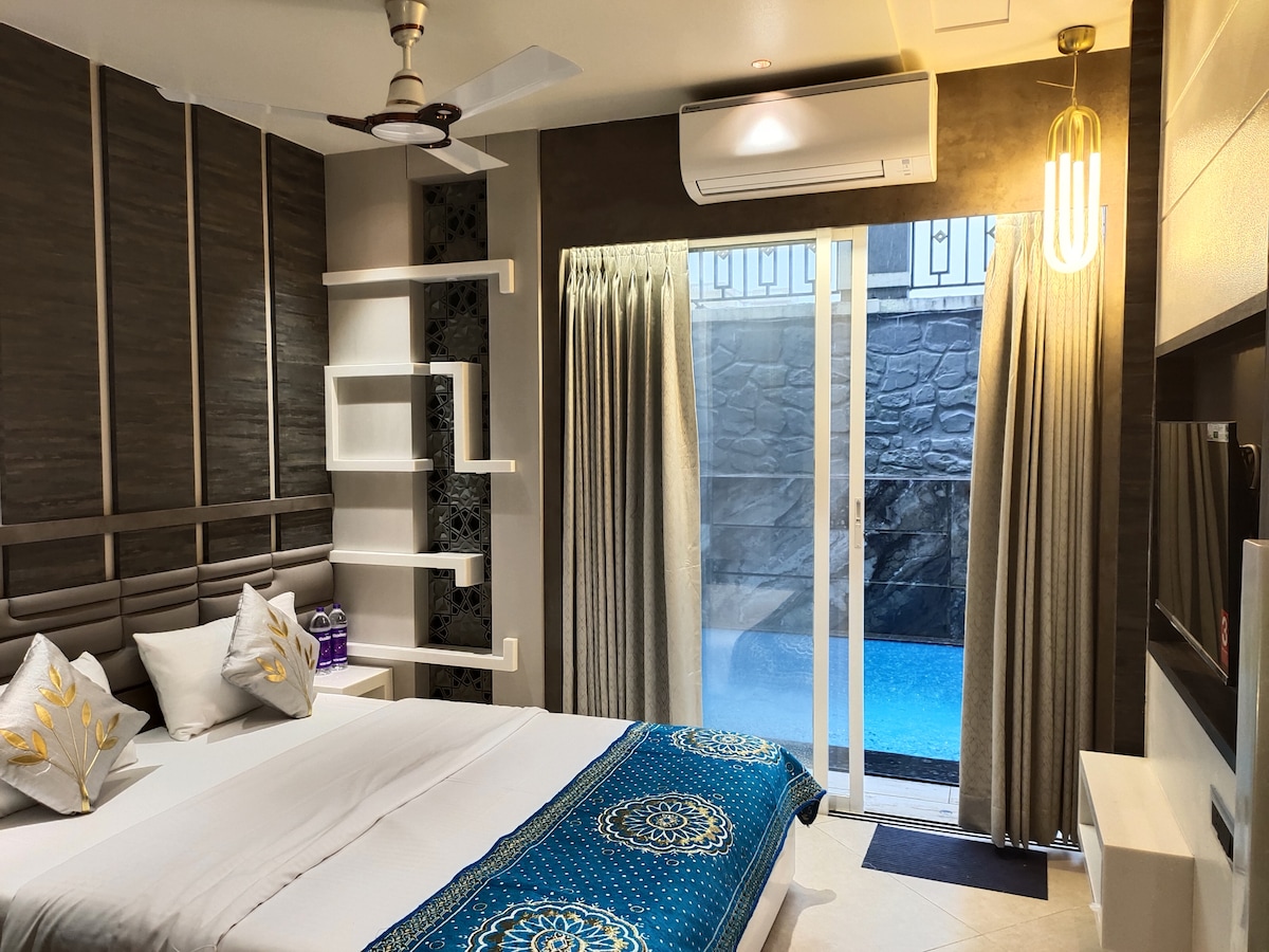 A well-appointed bedroom features a spacious bed adorned with decorative pillows. Natural light floods the room through large glass doors that provide direct access to a pool area. Textured wall panels and soft curtains complement the serene ambiance.