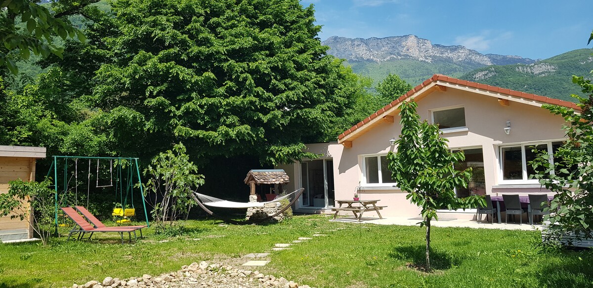 A spacious garden features a hammock and a picnic area with a table. Nearby, a swing set provides recreational options. Lush greenery surrounds the home, enhancing the outdoor experience, with mountain views in the background highlighting the natural setting.