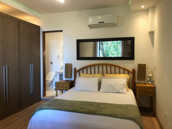 Byt Luxusný (apartmán 3 z 3): Apartmán s manželskou posteľou Queen, veľkou šatníkovou skriňou a mramorovou kúpeľňou s krabicou v pozadí. Posteľ má výhľad na les vpredu.