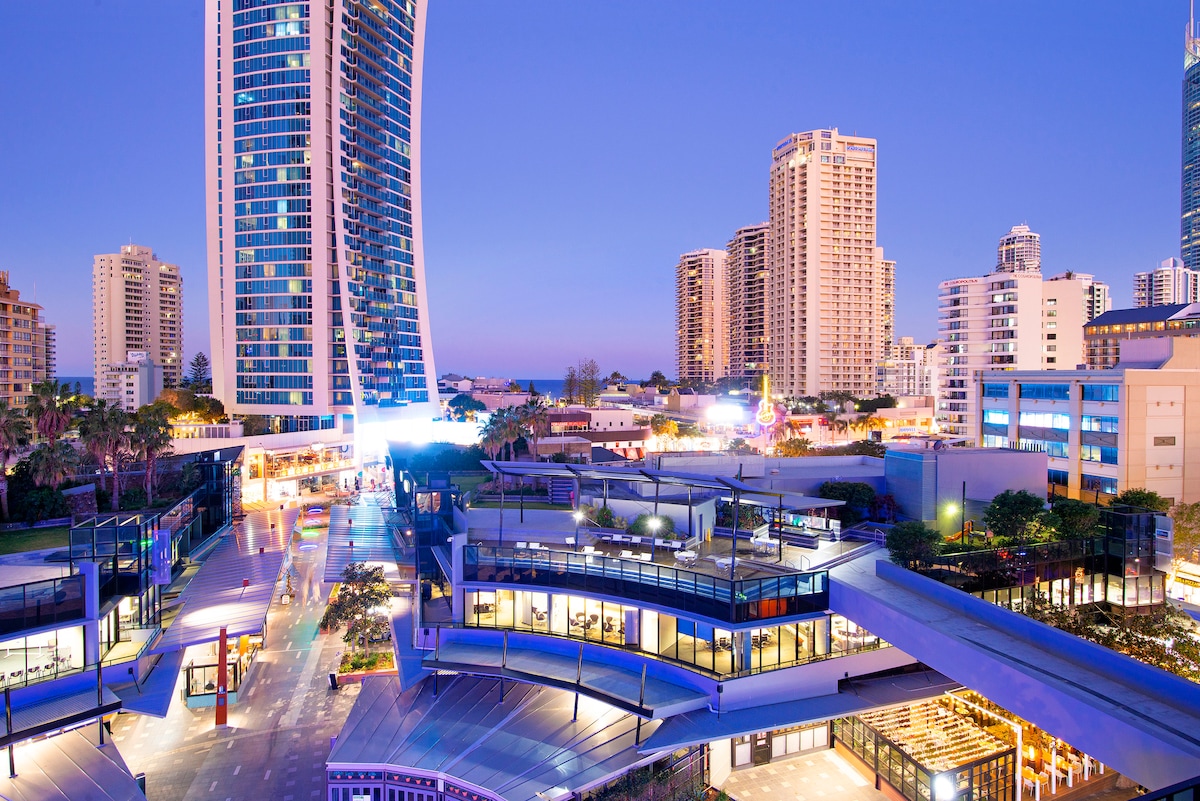 The image showcases the vibrant Circle on Cavill complex at dusk, featuring modern architecture and illuminated spaces. Several shops and restaurants are visible along with surrounding high-rise buildings, creating a lively atmosphere in the heart of Surfers Paradise.