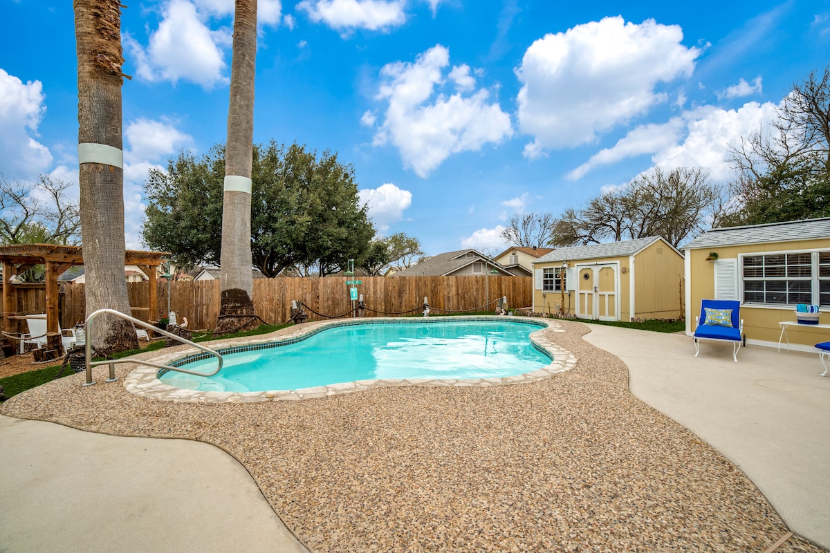 The inviting backyard features a sparkling pool surrounded by a textured patio and lush greenery. Tall palm trees provide shade, while a playhouse and gazebo complement the family-friendly environment. The space offers ample room for relaxation and leisure activities.
