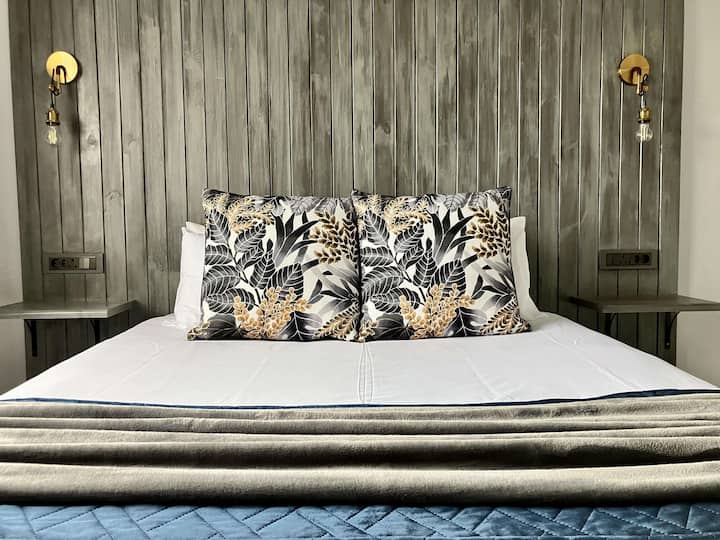 Serene Retreat: עם מיטת קווין סייז ומזגן עץ מהרצפה עד התקרה. אורות מיטת קיר מוזהבים מוסיפים חמימות ויוקרה לאווירה שלווה ומפוארת.