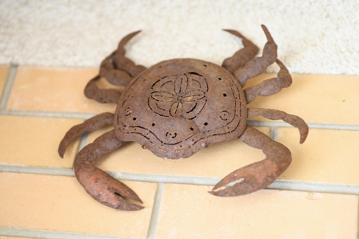 A decorative metal crab sculpture is mounted on a light-colored wall. The crab features intricate cut-out patterns and a rustic finish, providing a coastal-themed accent that complements the beach surroundings.