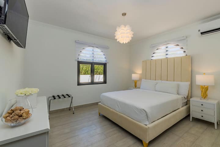 This bedroom has a king-sized bed, air-conditioning unit, a sleek nightstand, and an elegant tall headboard.