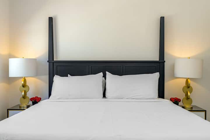  This bedroom has a king-size bed, decorated with a metal disc and brass plated Mid century modern table lamp on top of a wooden nightstand. Artistically designed headboard. Spacious and fully air-conditioned.