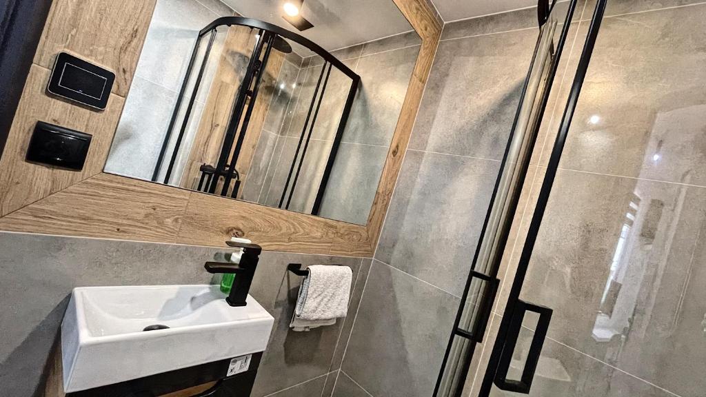 A modern bathroom is displayed, featuring a glass walk-in shower and a stylish mirror framed in light wood. A white sink is positioned beneath the mirror, with essential amenities nearby, including a towel hanging on a rack. Neutral tile colors create a sophisticated ambiance.