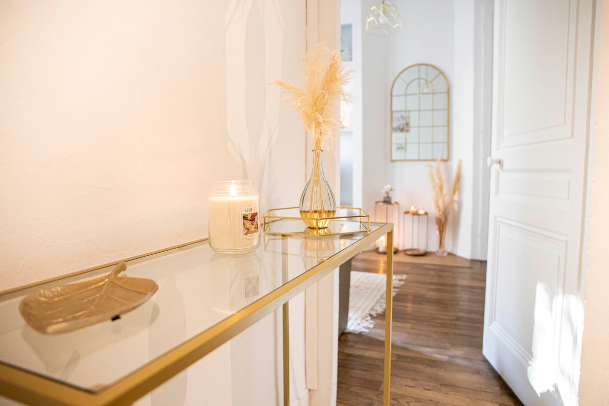 A stylish console table is positioned against a white wall, featuring a glass top with a decorative dish and a lit candle. A simple vase with dried flowers adds a touch of elegance, while a framed mirror reflects warm light, enhancing the welcoming ambiance of the hallway.