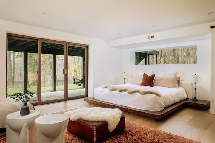 Downstairs bedroom boasts a comfortable king bed, private bathroom with shower, and its own lounge space with sectional sofa and smart TV. Private entrance leads directly to a stone patio with a porch swing overlooking the lawn, fire pit and pond. 