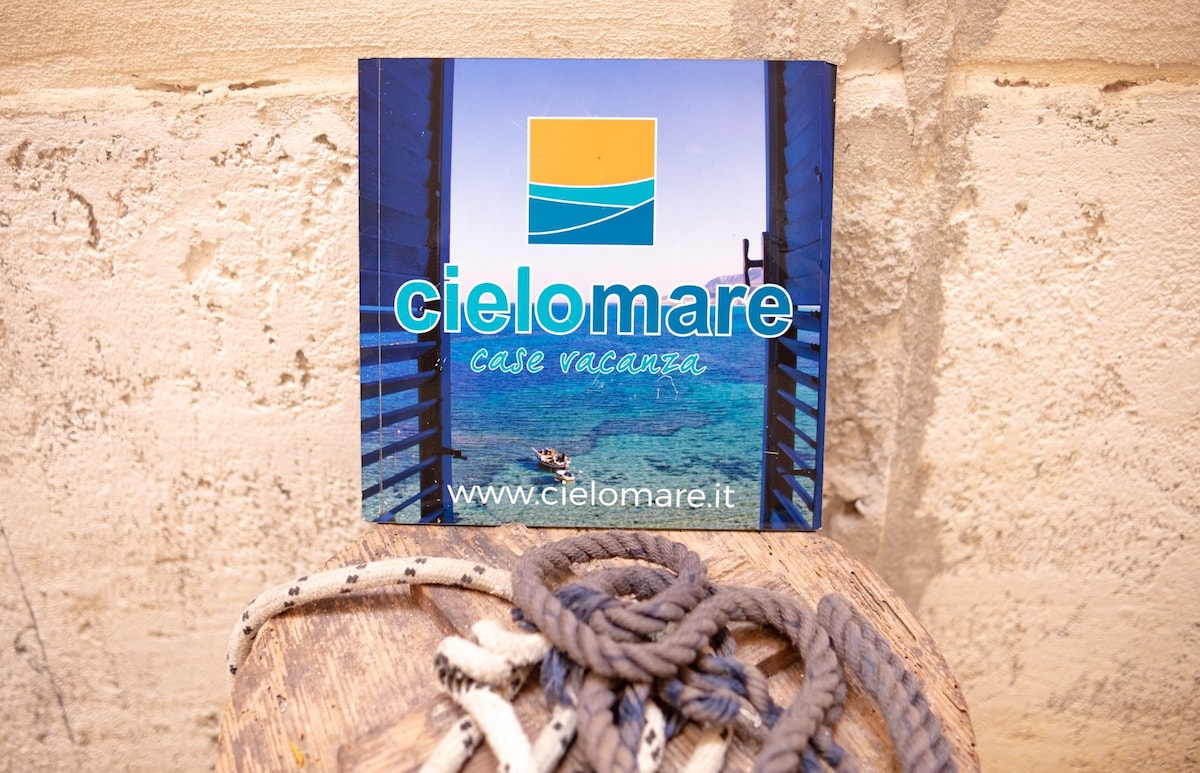 A promotional sign for Cielomare is presented, featuring a vibrant image of turquoise waters and a graphic logo. The sign is positioned against a textured wall, complemented by nautical ropes in the foreground, adding a coastal theme to the scene.