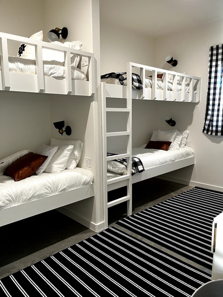 غرفة بطابقين تحتوي على 4 أسرّة كبيرة جدًا وتلفزيون ذكي. 