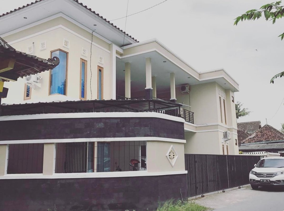 The exterior of a two-story building is presented, showcasing a combination of light and dark tones. Large windows allow natural light to fill the space, while a covered balcony is visible on the second floor. A car is parked in front, adding a sense of accessibility.