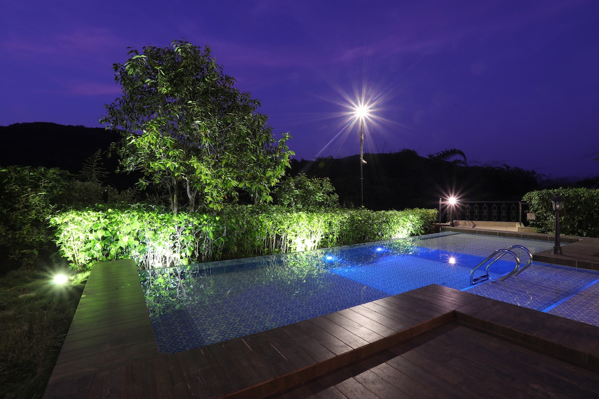 A private pool is surrounded by lush greenery, with soft lighting illuminating the water and nearby plants. The serene atmosphere is enhanced by a clear evening sky, providing a peaceful retreat for relaxation.