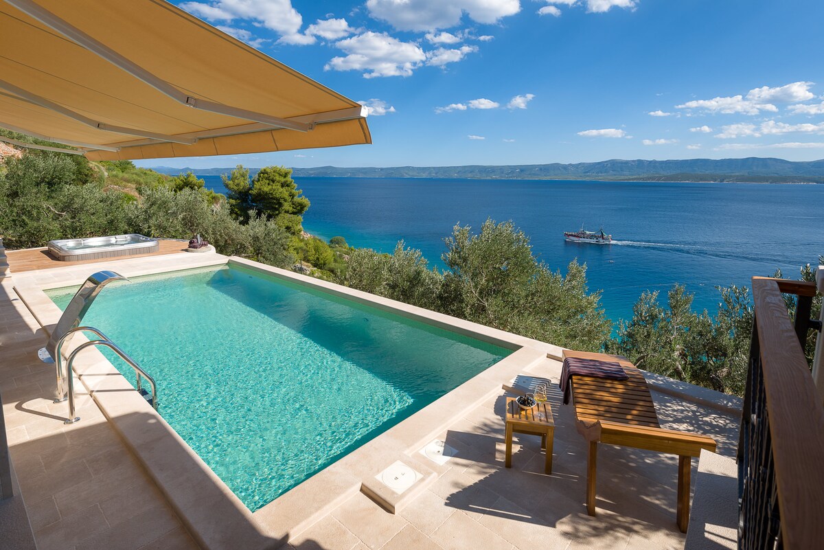 An inviting outdoor area features a clear swimming pool with a sleek edge, set against a backdrop of the Adriatic Sea. A comfortable lounge chair and a small side table are positioned nearby, along with a hot tub. The scene is framed by lush greenery and a vibrant sky.