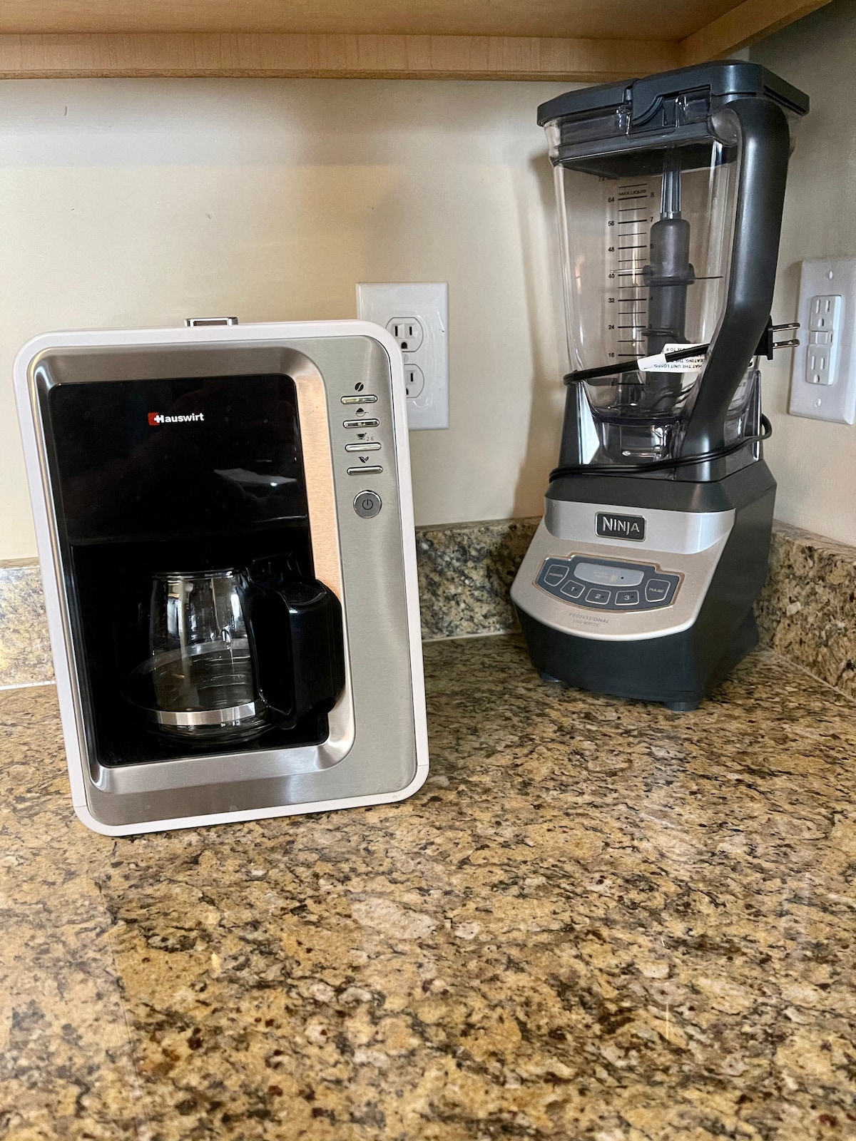 A sleek coffee maker is positioned beside a high-performance blender on a granite countertop. The coffee maker features a glass carafe, while the blender has an easy-to-read control panel, offering convenience for meal preparation and beverage making in the kitchen.