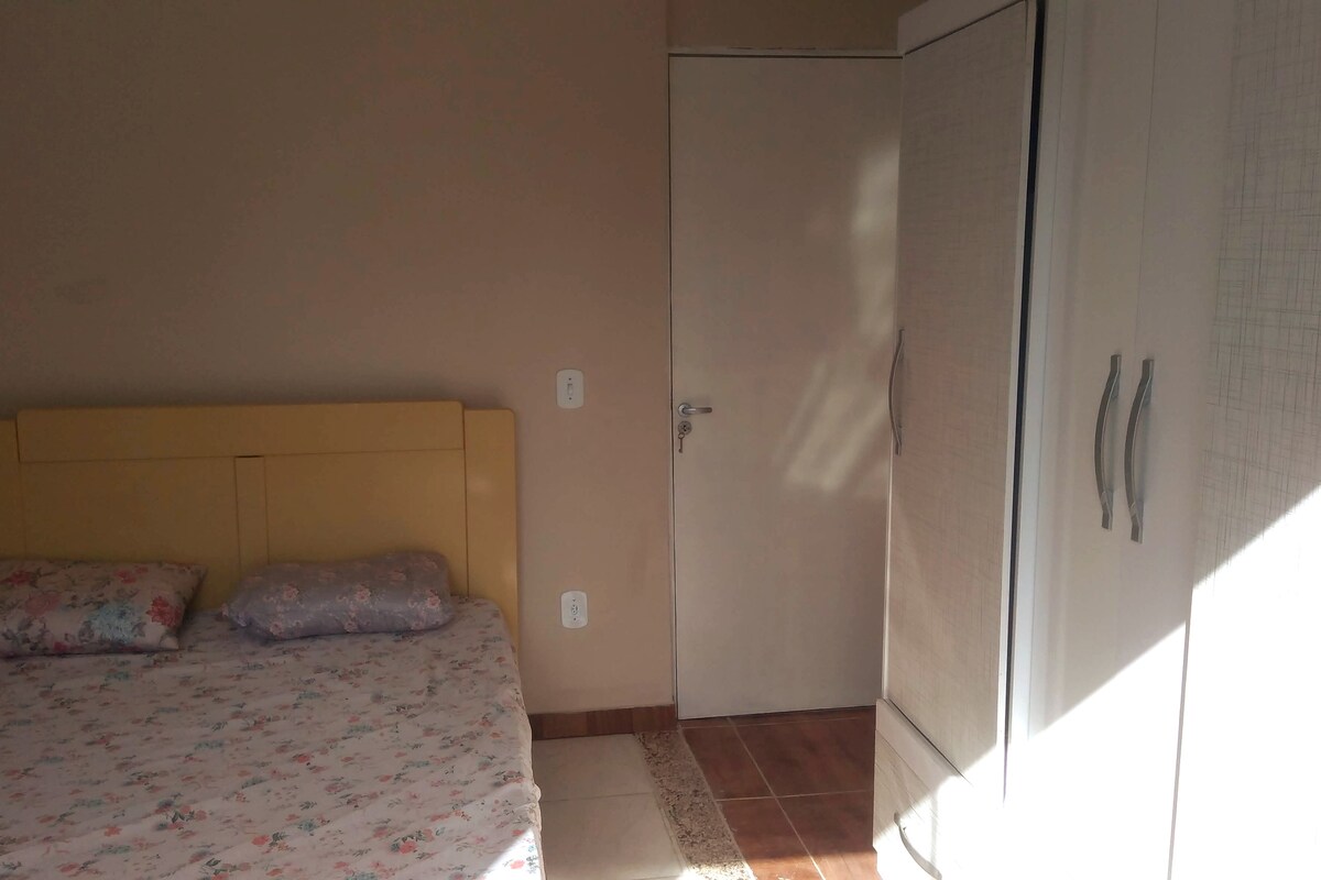 Quarto com cama de casal, ventilador e guarda roupas.
Vista para os fundos da casa. 