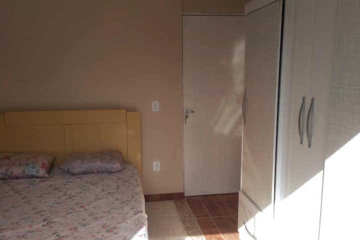 Quarto com cama de casal, ventilador e guarda roupas.
Vista para os fundos da casa. 