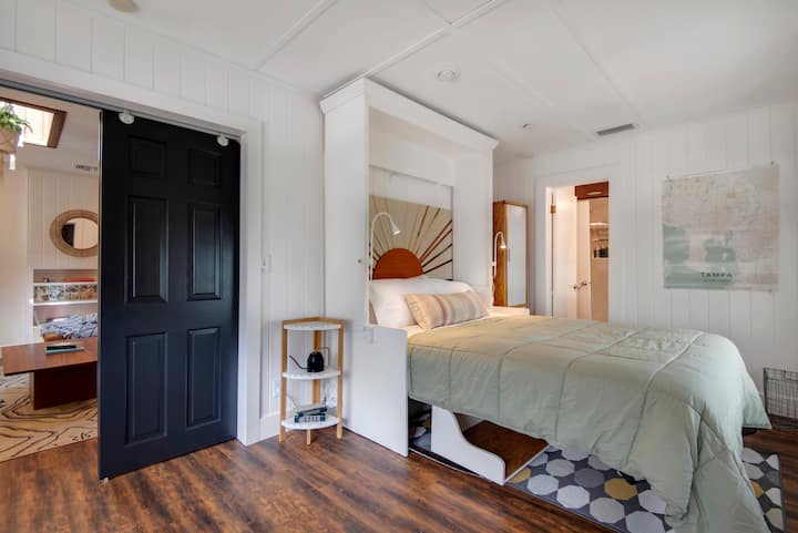The third bedroom is located off of the living room, and the black doors close for privacy. There are reading lights and plugs on the side of the Murphy bed, and the wardrobe to the right of the bed includes hanging space. 