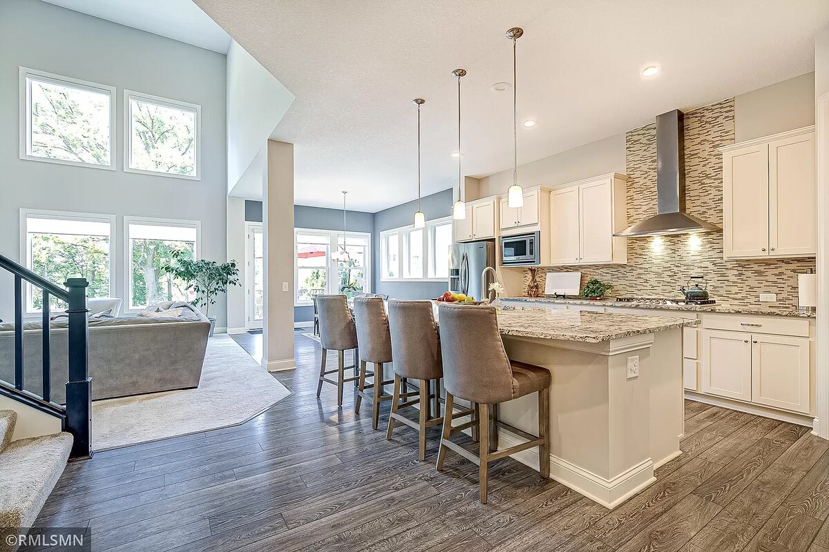 The kitchen is designed with modern fixtures, featuring a large island with bar seating for four. Natural light streams in through multiple windows, highlighting the granite countertops. The space is complemented by light cabinetry and stylish tile accents, creating an inviting atmosphere for cooking and gatherings.