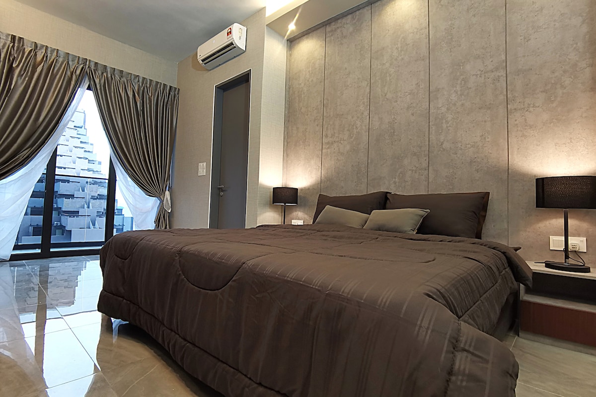 A comfortable sleeping area features a spacious bed covered in a rich brown duvet, complemented by matching pillows. Soft lighting from bedside lamps illuminates the grey accent wall. A large window offers a view of the outside, framed by elegant curtains.