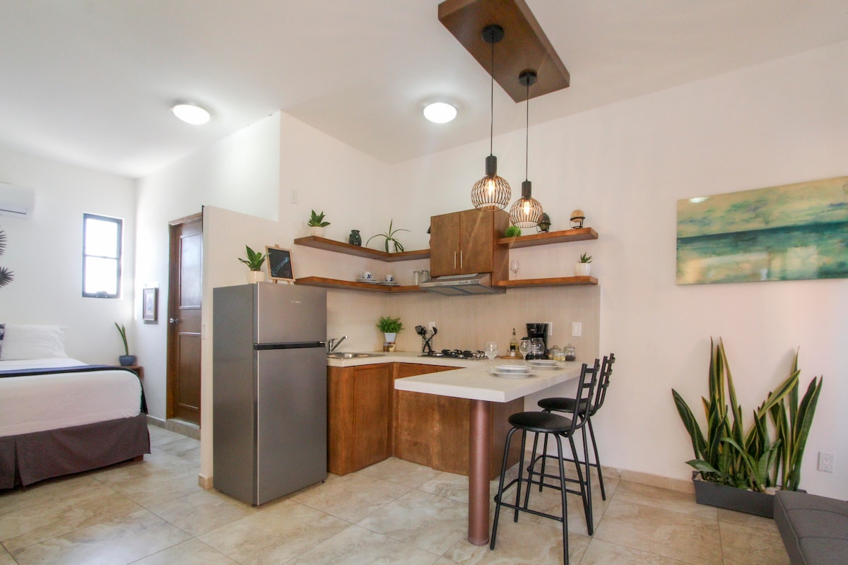 A well-equipped kitchen area is featured with modern appliances and a small dining space. The loft includes a spacious bed and is complemented by natural light filtering through the window. Decorative plants add a touch of greenery to the ambiance.