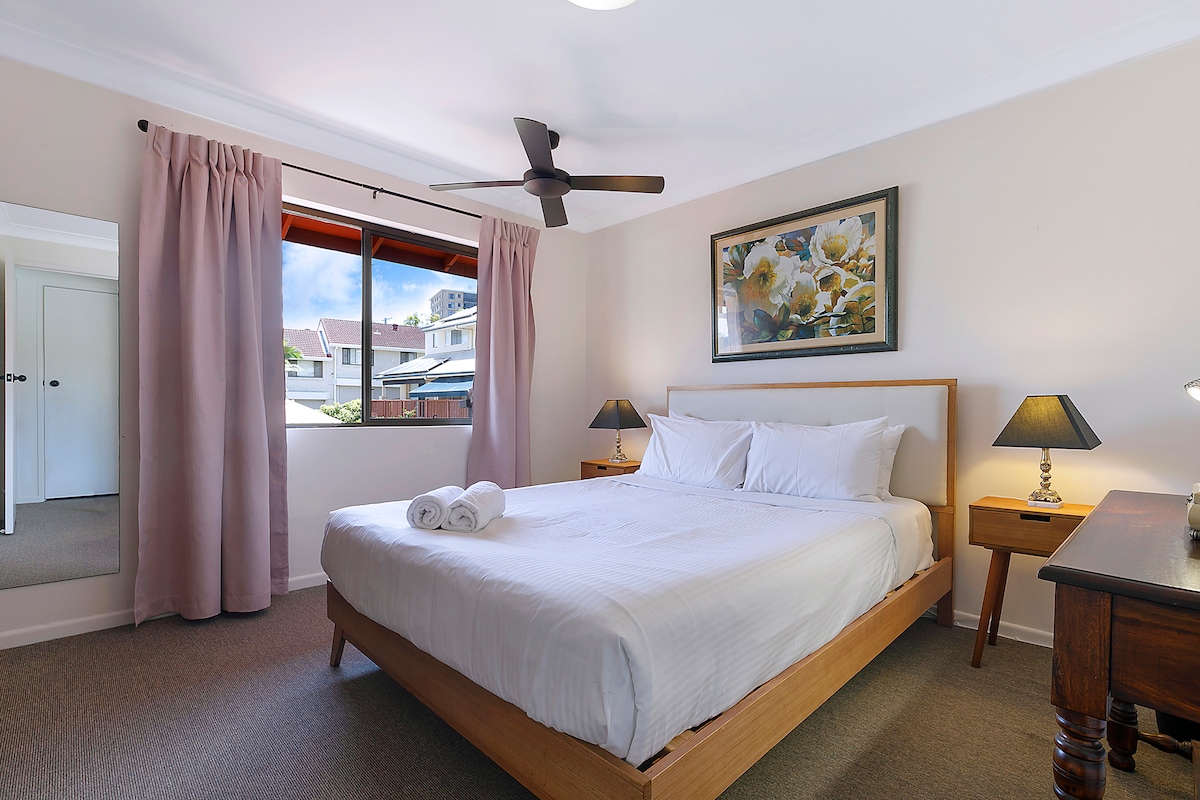 ห้องนอนใหญ่ตกแต่งด้วยเตียงควีนไซส์หรูหราพัดลมเพดานและหน้าต่างบานใหญ่พร้อมวิว
