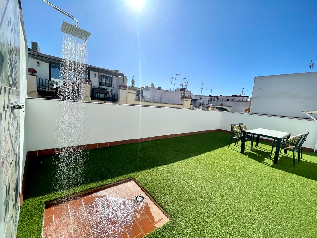 A private terrace features artificial grass and a dining table with chairs, providing a comfortable outdoor space. An outdoor shower is installed, allowing for refreshing experiences under clear skies. The area is well-lit, enhancing the overall atmosphere of relaxation.