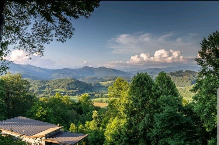 A panoramic view of the Smoky Mountains is captured, showcasing rolling hills and lush greenery under a clear sky. The landscape is dotted with trees, and the distant mountains create a serene backdrop.