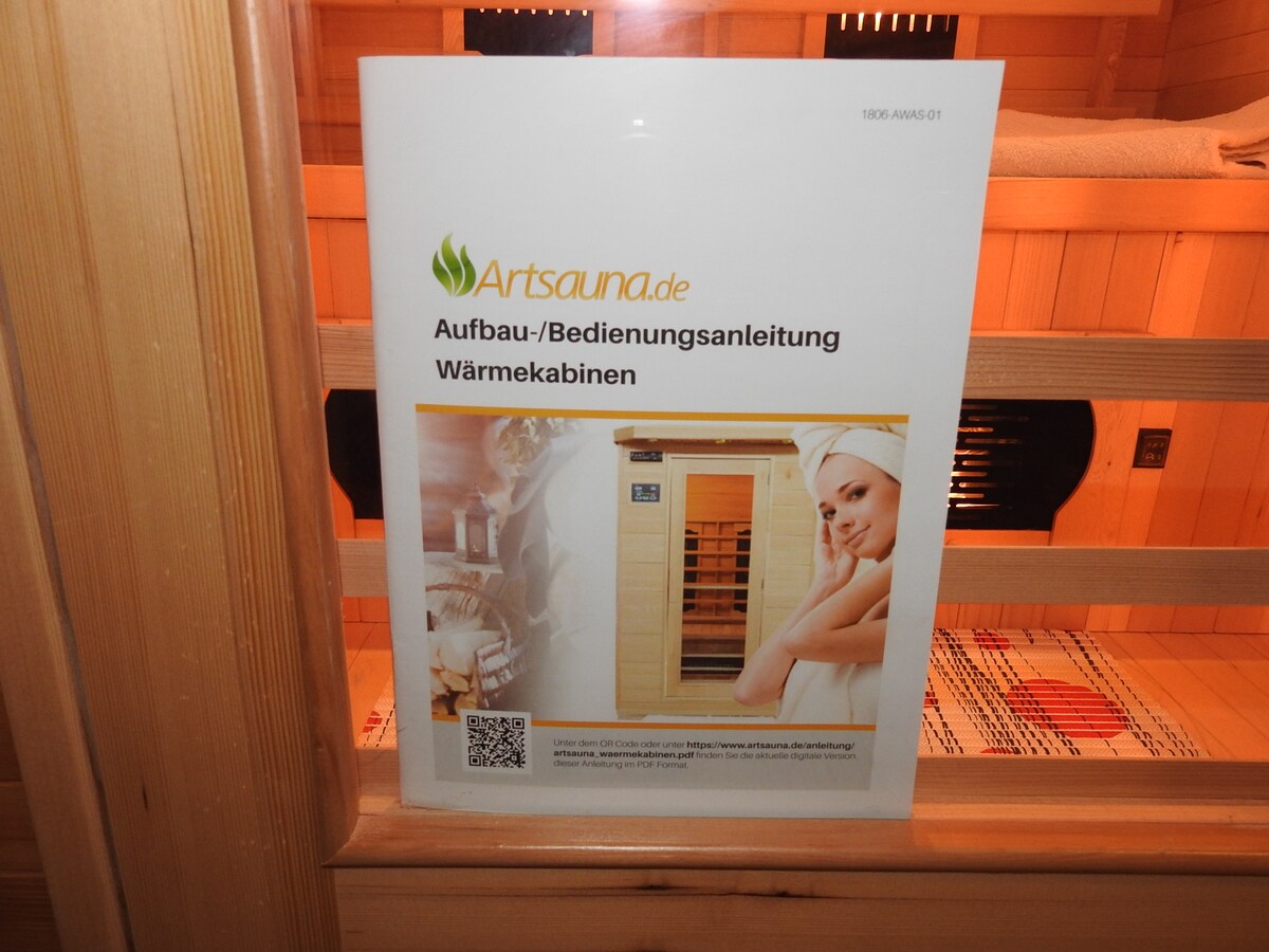 An informational sign regarding the setup and operation of a sauna is visible. The sign features clear text in German, alongside a simple image illustrating sauna usage. The wooden interior of the sauna is partially visible in the background, showcasing the relaxing environment.