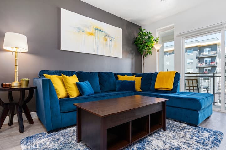 Ლამაზად მოწყობილი მისაღები ოთახი. 65‑დუიმიანი Roku‑ტელევიზორი, ფერადი სექციური დივანი და მთებისა თუ ქალაქის ხედები.