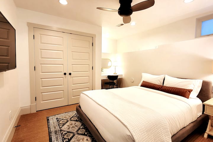 غرفة نوم بحجم كوين في الطابق السفلي مع تلفزيون ذكي ومكتب عمل وشرفة سقف.