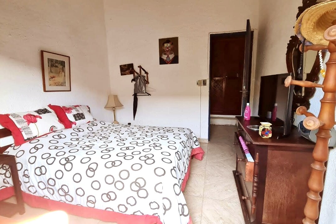 Habitación con cama doble con ventilador de techo, cómoda y perchero y mesas laterales.