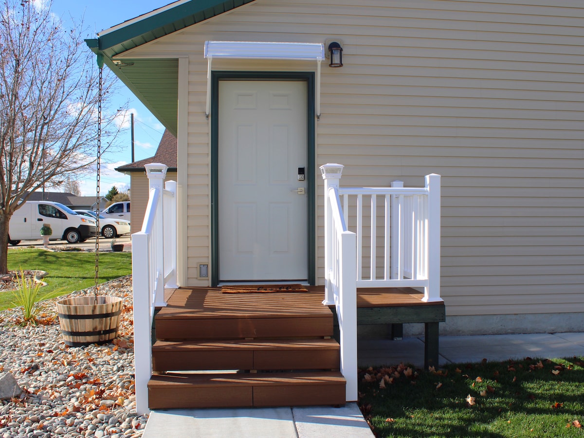 The entrance features a welcoming front porch with wooden steps leading up to a solid door framed by white railings. A light fixture is positioned to the side for evening illumination, while a doormat is placed at the door's threshold.