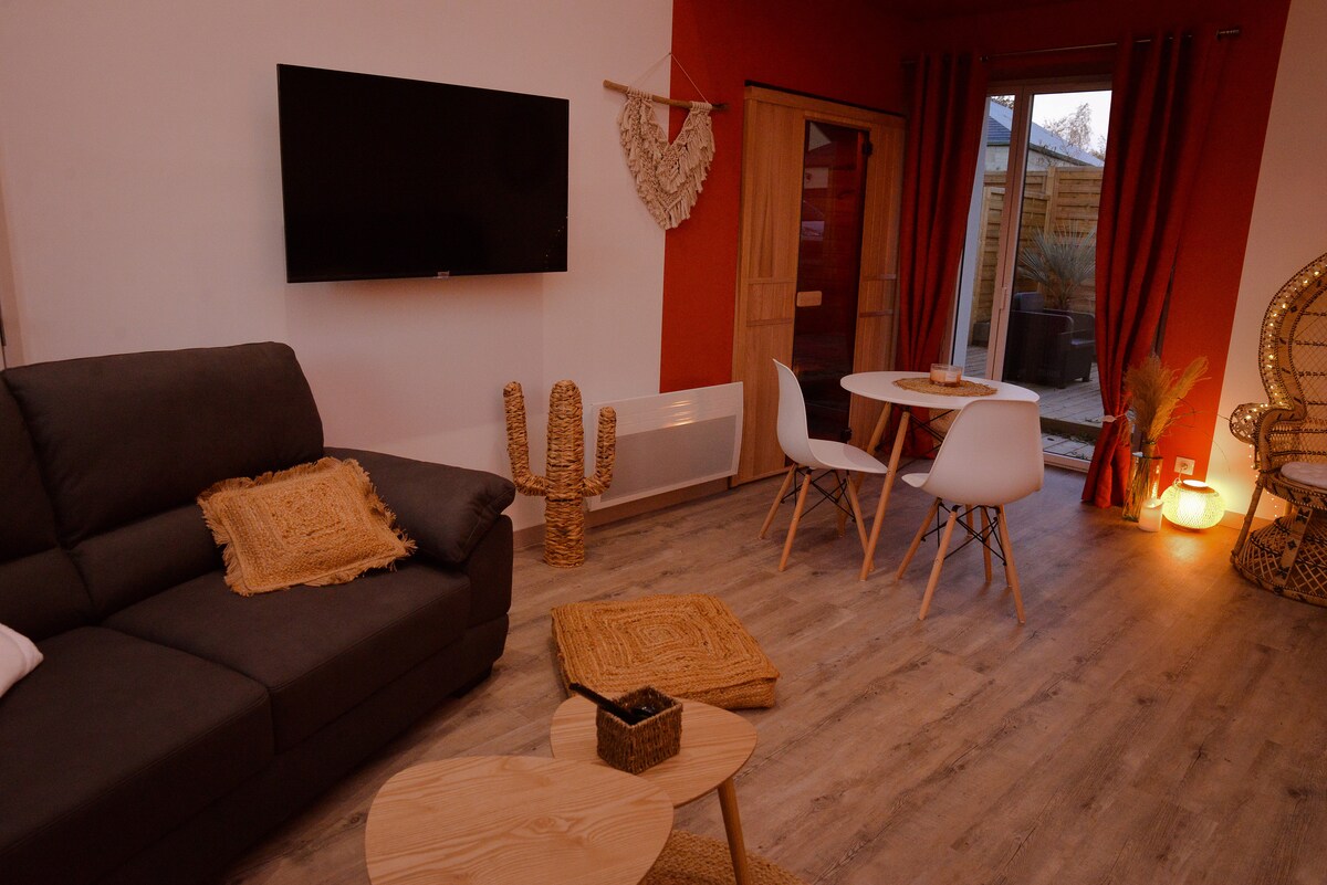 A modern living area features a dark sofa complemented by woven decor and light wood furniture. A round dining table with white chairs is positioned near a door opening to an outdoor space. Soft lighting creates a comfortable ambiance, enhancing the cozy atmosphere.