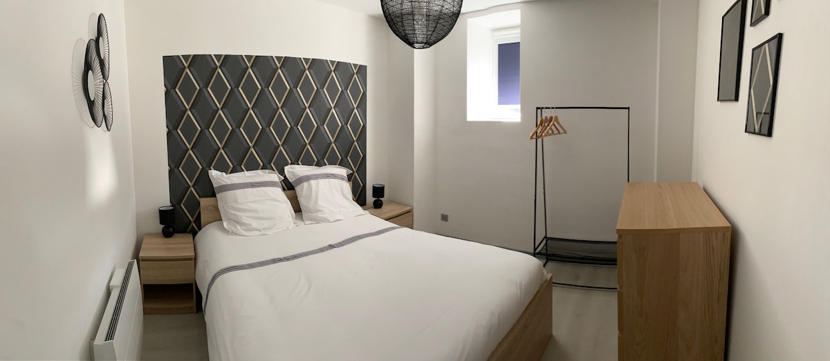 A minimalist bedroom features a spacious bed with white linens and decorative throw pillows. A geometric headboard adds texture, while a clothing rack and wooden dresser provide storage options. Soft lighting from bedside lamps creates an open and bright environment.