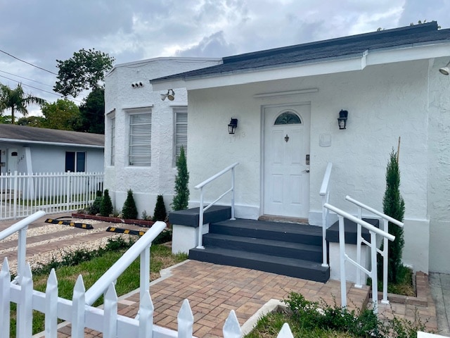 A freshly remodeled entrance is showcased with a white exterior and a prominent door. Flanking the door, two small shrubs provide greenery. The steps leading to the entrance are framed by a white railing, while a paved walkway guides guests from the driveway.