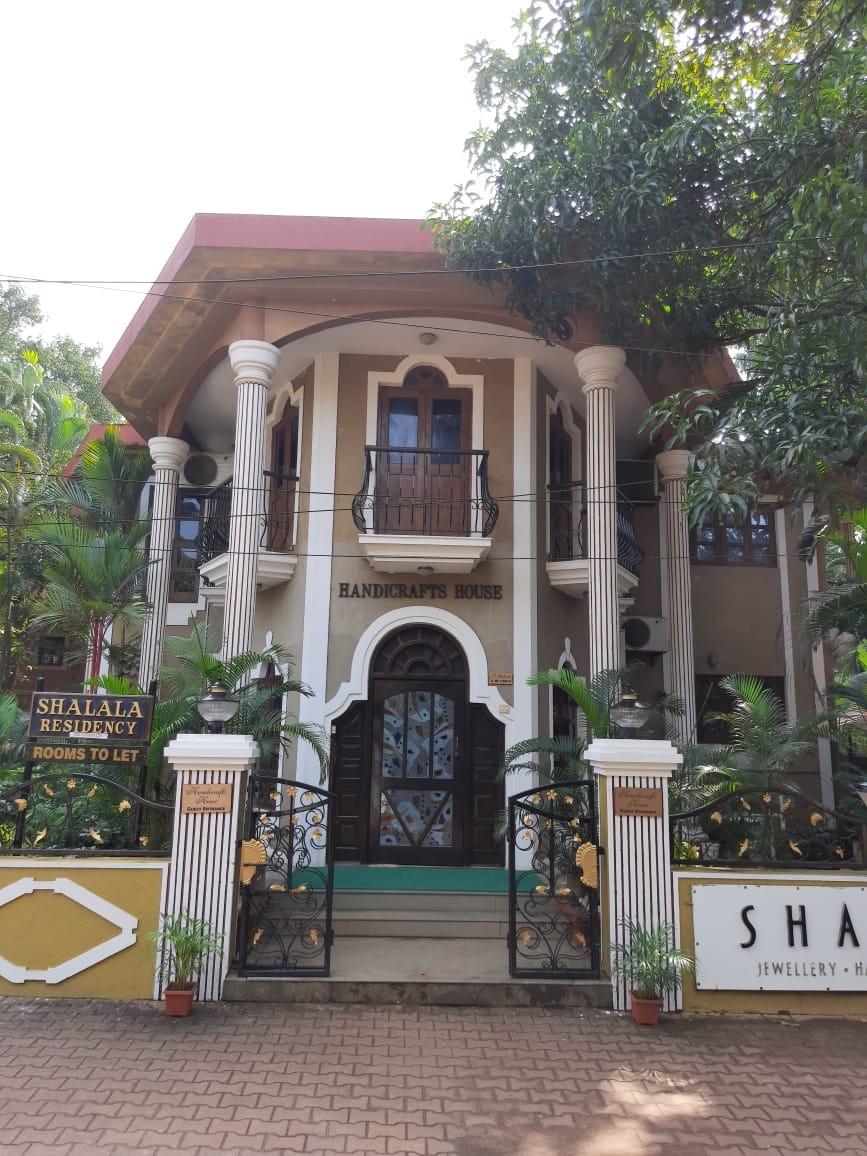 The entrance of Shalala Residency is framed by columns and flanked by lush greenery. A sign in front designates the residence, while a staircase leads up to an inviting double-door entry. The building showcases a blend of traditional and modern architectural elements.