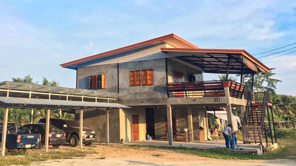 A two-story building is featured, displaying an open balcony and a covered parking area. Large windows are positioned on the upper level, allowing natural light to enter. A staircase leads to the balcony, enhancing accessibility to outdoor views.