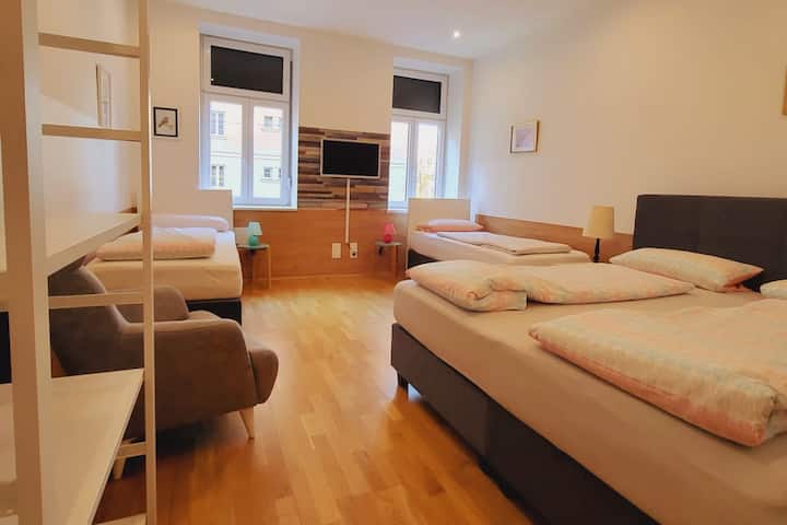 1re chambre avec un grand lit double, 2 lits simples, télévision intelligente, un fauteuil confortable et une armoire ouverte