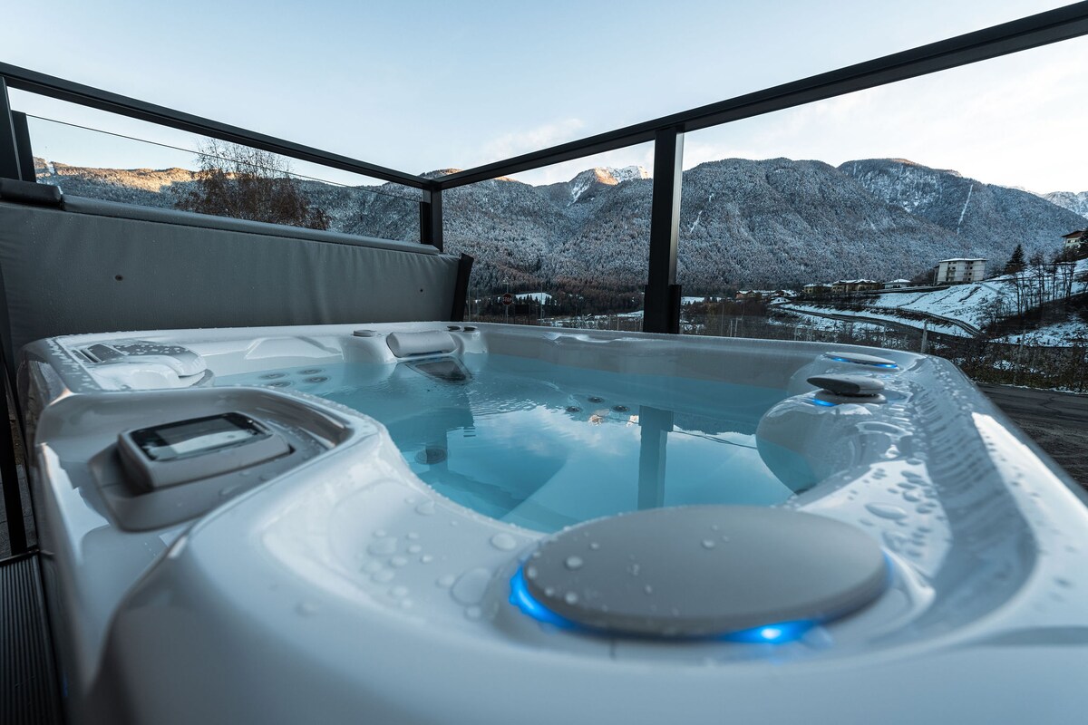 A hot spring on the terrace is featured, with water reflecting the surrounding snow-capped mountains. The spacious design includes built-in seating and subtle LED lighting, creating a serene and inviting atmosphere against the backdrop of a winter landscape.