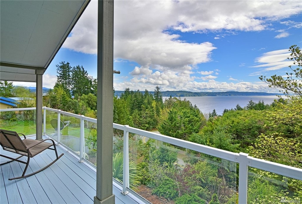A spacious deck features a railing and two lounge chairs, offering a clear view of the lush greenery and serene water beyond. The sky is partly cloudy, providing a cool and inviting atmosphere for outdoor relaxation.