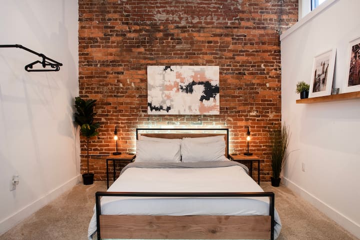 La gran cama tamaño queen con colchón Casper y una gran pared de ladrillo crean un ambiente acogedor