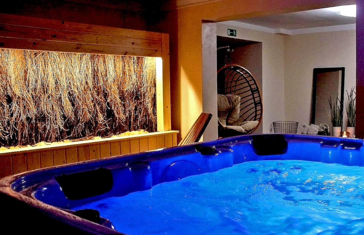 A private spa area is highlighted by a large, inviting jacuzzi filled with sparkling blue water. A decorative wall with natural elements is visible in the background, while a cozy seating area is partially seen on the right, enhancing relaxation options.