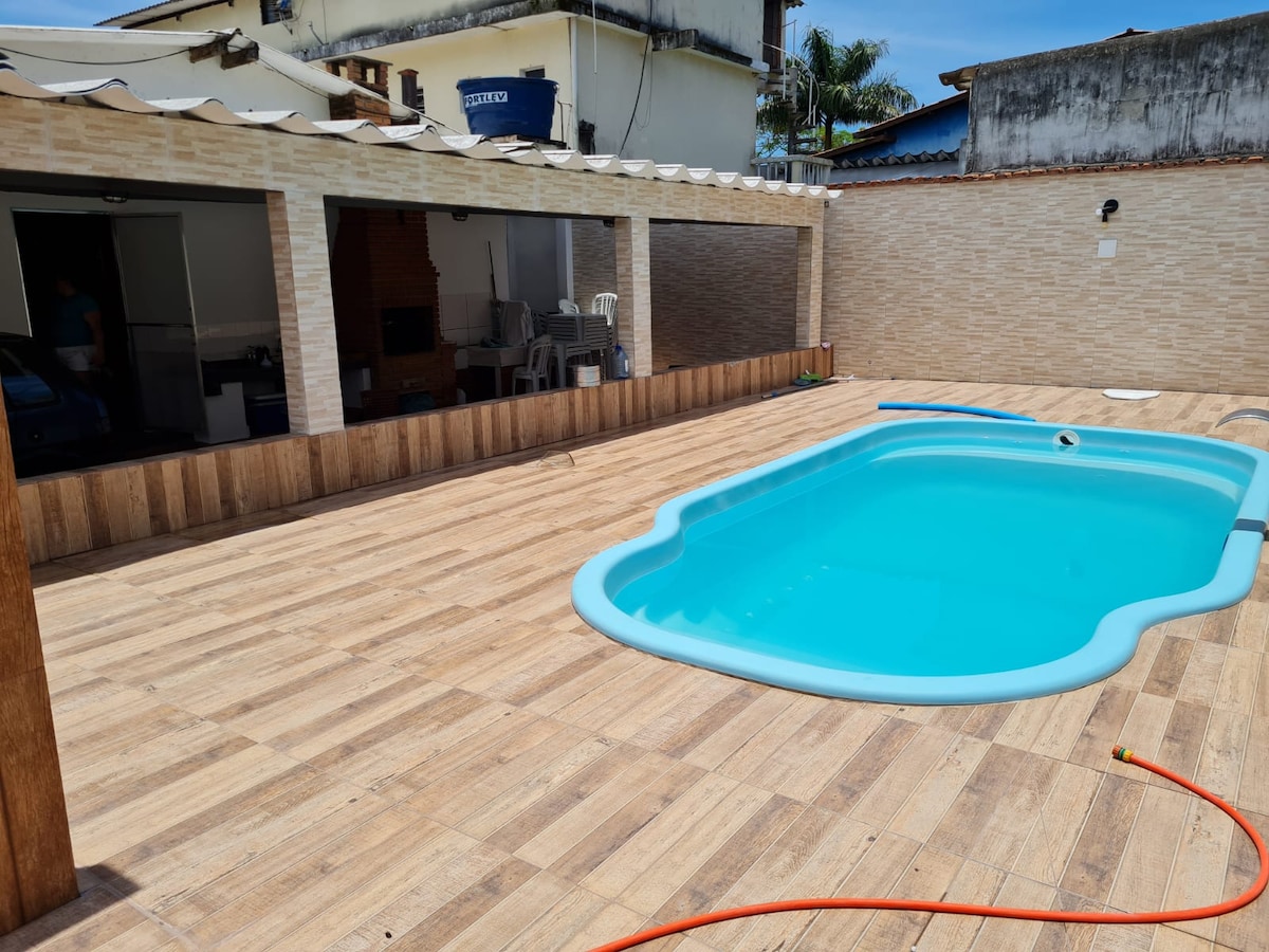 An outdoor area features a refreshing pool surrounded by wooden decking. Comfortable seating is visible under a shaded space, providing options for relaxation. The area is well-lit, with a clear view of the surrounding structures and landscaping complementing the ambiance.