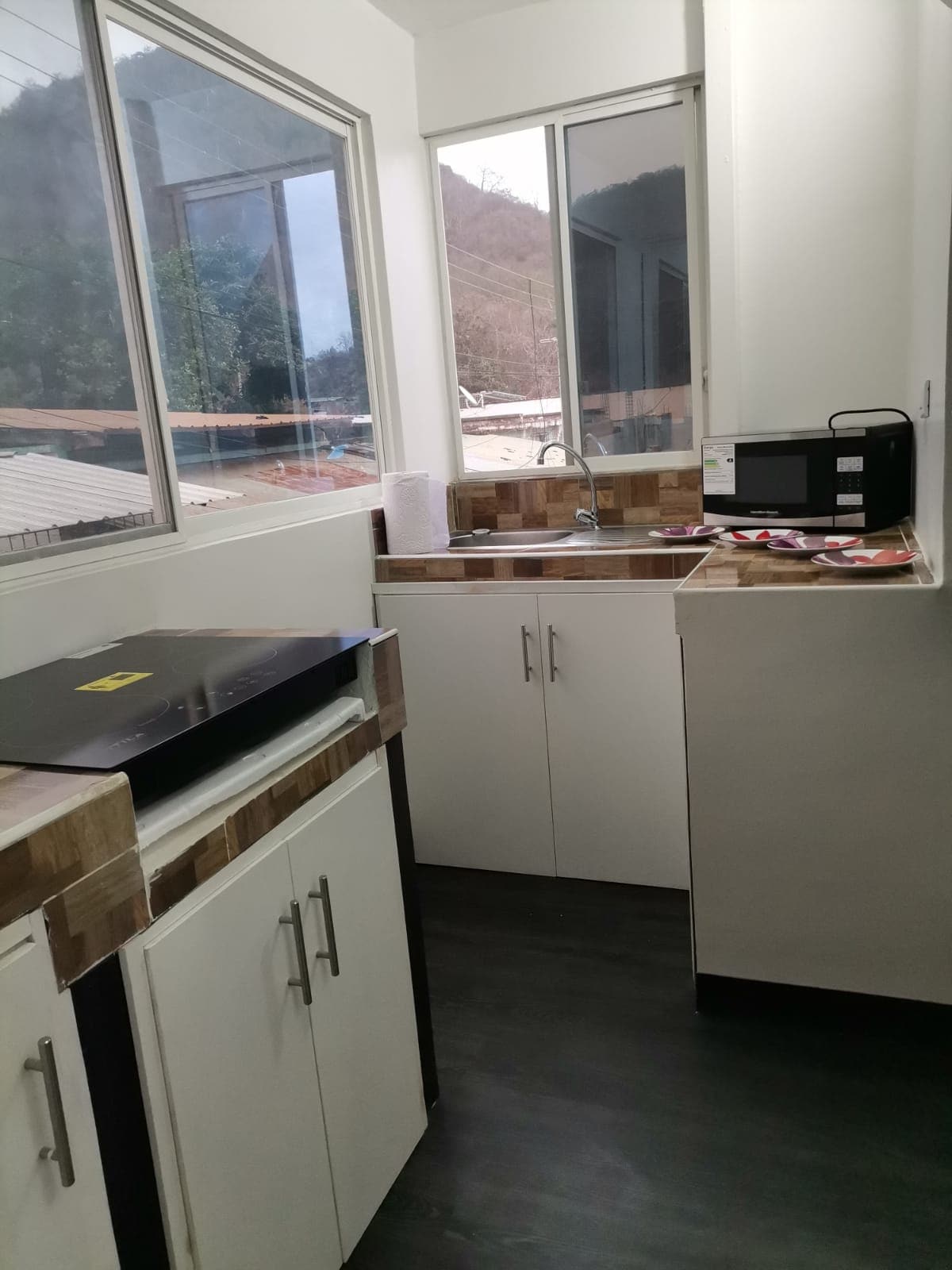 The kitchen is designed with modern cabinetry and includes a sink, microwave, and counter space. Large windows provide natural light and showcase views of the surrounding area, enhancing the overall functionality of the space.