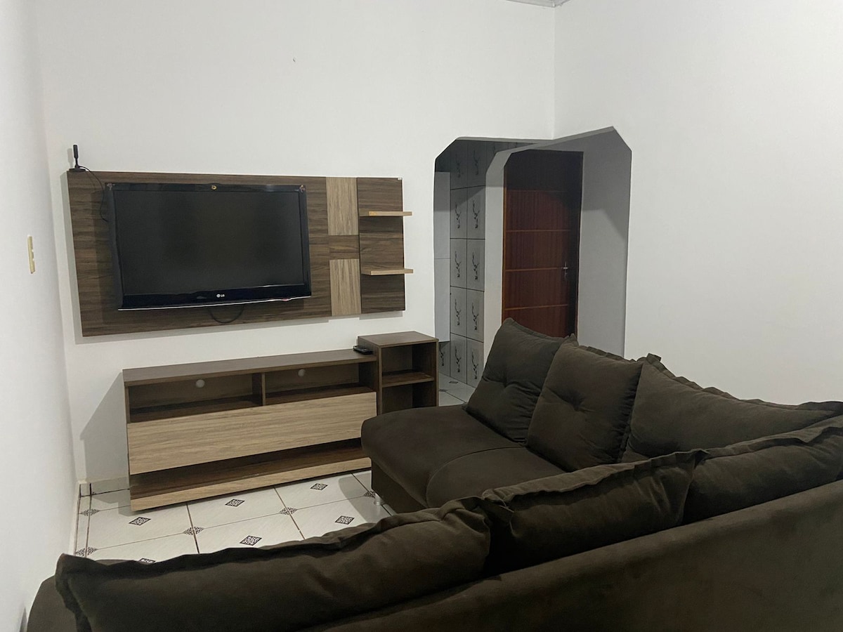 A comfortable living area features a sectioned sofa in earth tones, positioned across from a wall-mounted television. The sleek entertainment unit holds decorative items and offers storage, while patterned tiles enhance the floor's visual interest. A doorway leads to another room in the background.
