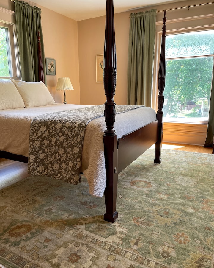 Upstairs bedroom with queen four post bed and a sitting chair to relax or read.
