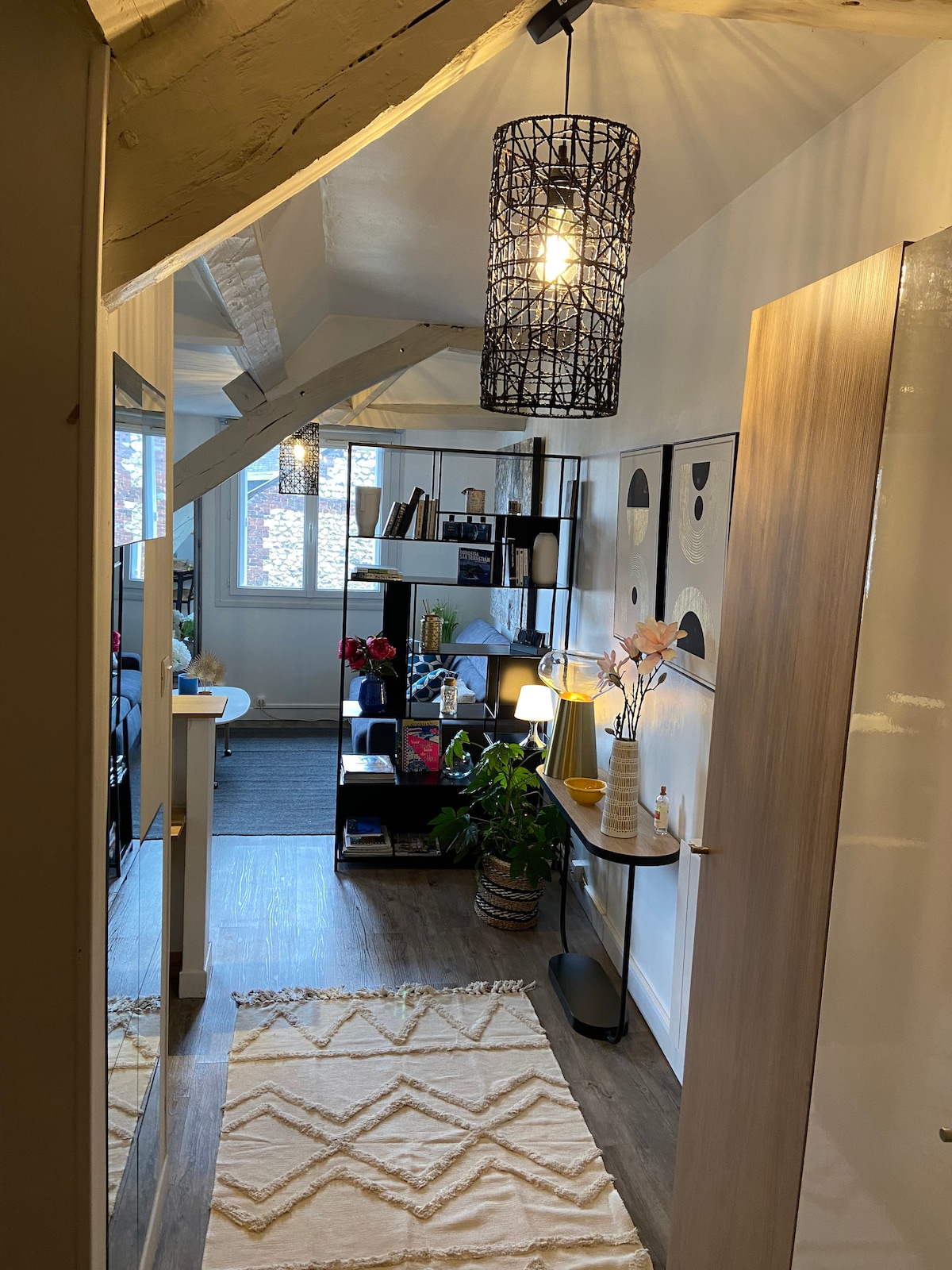 This entryway features ample natural light from multiple windows, with modern shelving displaying potted plants and décor. A console table is placed against the wall, complemented by a decorative lamp and artwork. A textured rug covers the floor, adding warmth to the space.