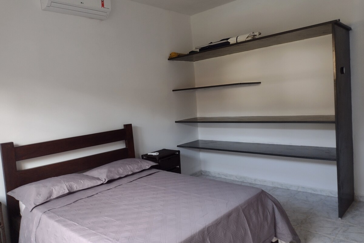 Suite en el dormitorio con cama doble, mesitas de noche, aire acondicionado y estantes para guardar artículos personales.