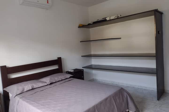 Spavaća soba s bračnim krevetom, noćnim ormarićima, klima-uređajem i policama za odlaganje osobnih stvari.