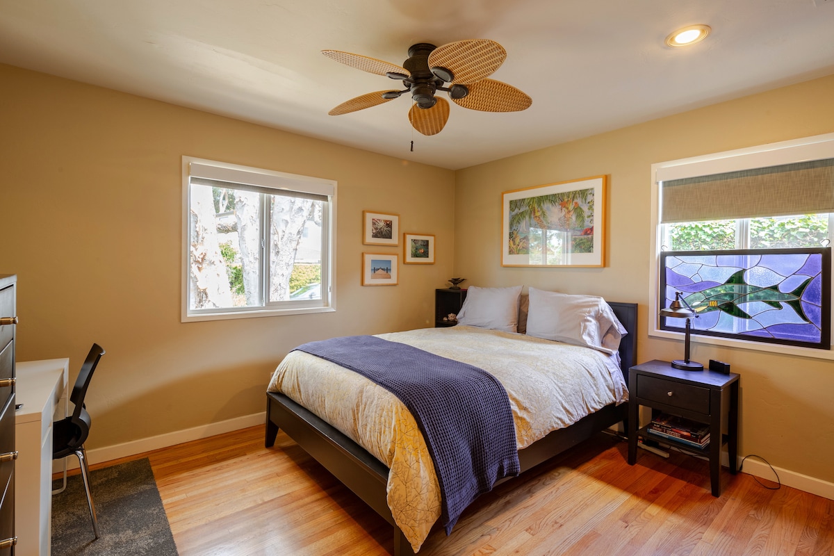 Bedroom 2: Queen Bed. Inviting guest bedroom with cozy bedding, ceiling fan, and natural light - featuring colorful artwork and a peaceful, homey atmosphere.